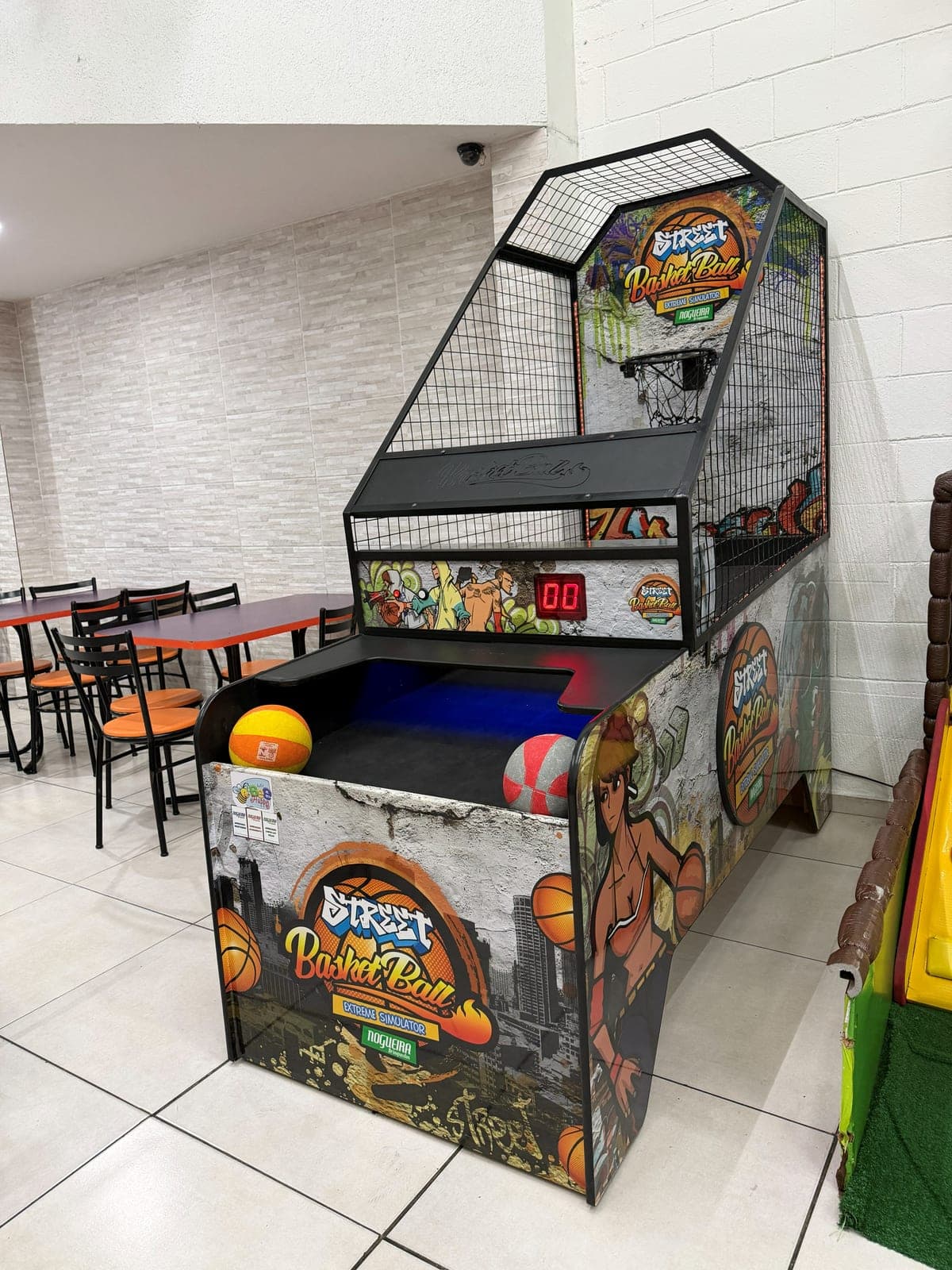 Máquina de basquete arcade com bolas, ao lado das mesas do salão