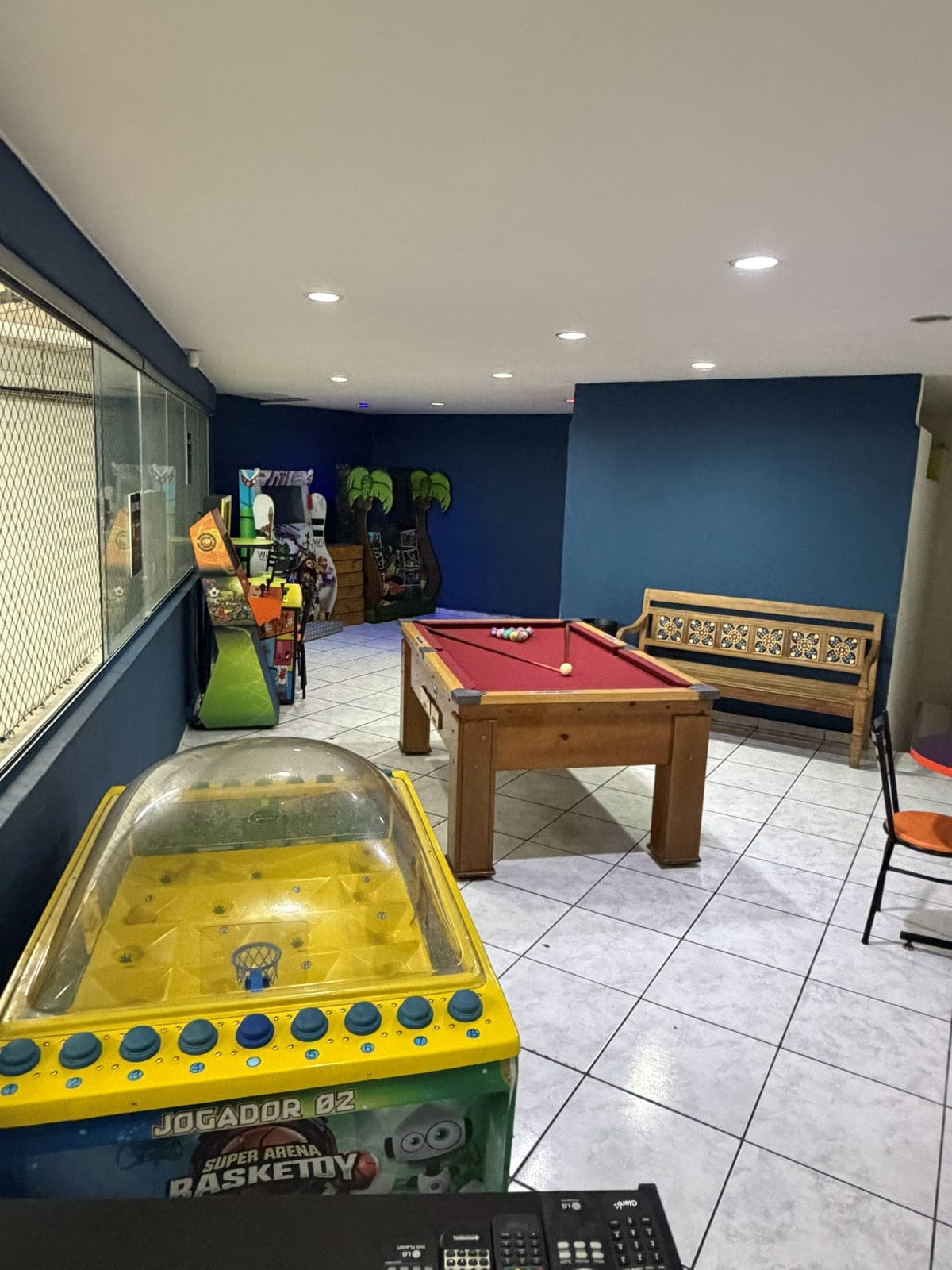 Sala de jogos com fliperamas, mesa de sinuca e banco de madeira